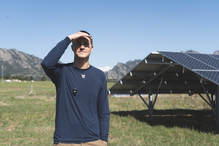 Man facing the camera in sunlight on a green field in front of solar panels